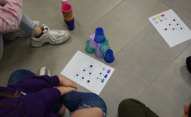 młodzież ukłąda wieżę z kolorowych kubeczków według wzoru z kartki