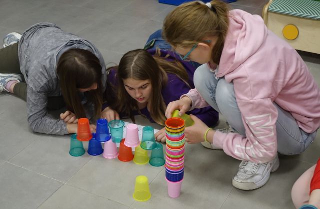 dzieci i młodzież siedzą na podłodze i ukłądają kolorowe kubeczki