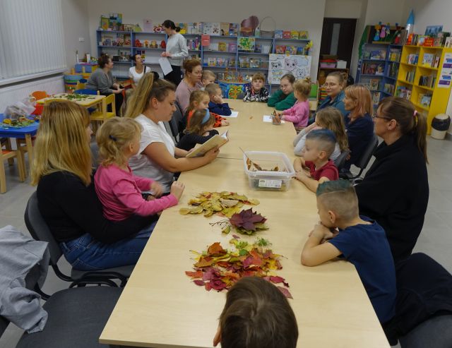 uczestnicy warsztatów siedzą przy stołach, bibliotekarka czyta książkę