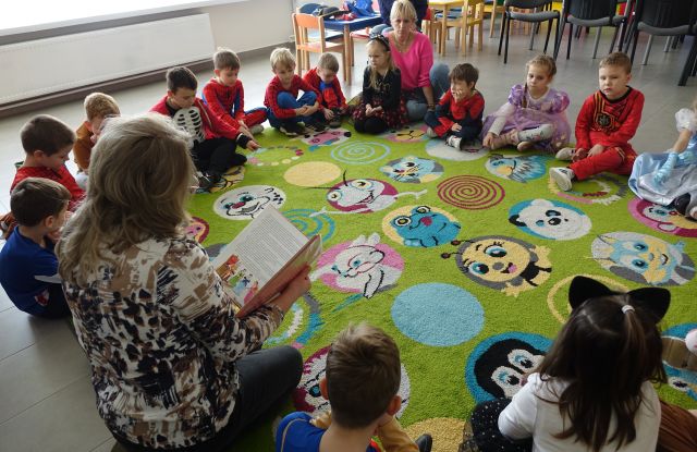 kobieta czyta dzieciom siedzącym na kolorowym dywanie, przebranym za postacie z bajek