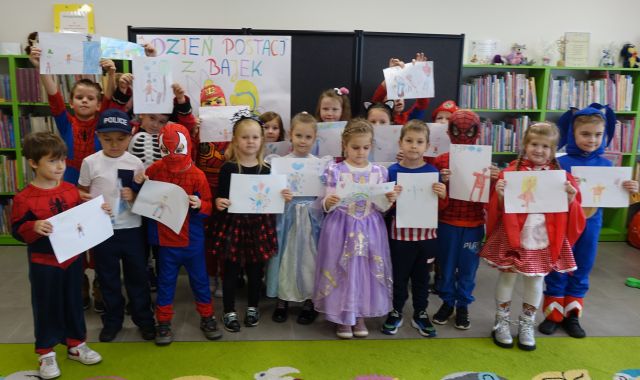 przedszkolaki przebrane za postacie z bajek pozują do zdjęcia z wykonanymi przez siebie ilustracjami