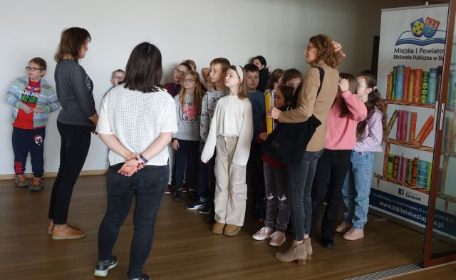 uczniowie stoją w holu biblioteki i słuchają bibliotekarki