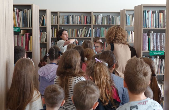 uczniowie spacerują pomiędzy regałami z książkami