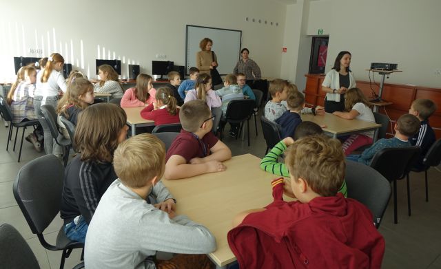 uczniowie siedzą przy stolikach w sali komputerowej