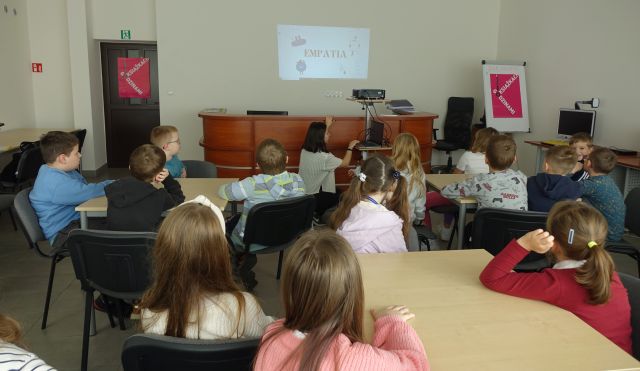 uczniowie siedzą przy stolikach w sali komputerowej i słuchają wykładu bibliotekarki