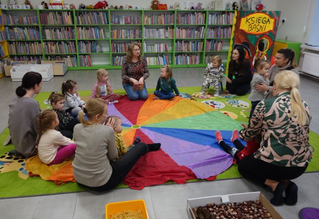 dzieci i rodzice siedzą wokół kolorowej chusty animacyjnej