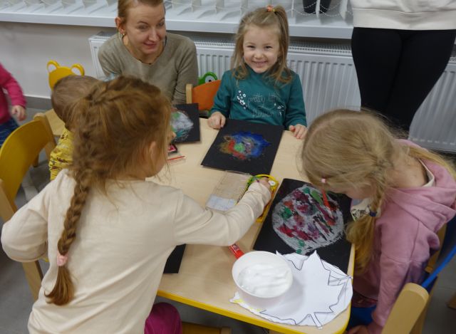 dzieci zamalowują liście na czarnych kartkach papieru kolorowymi farbkami