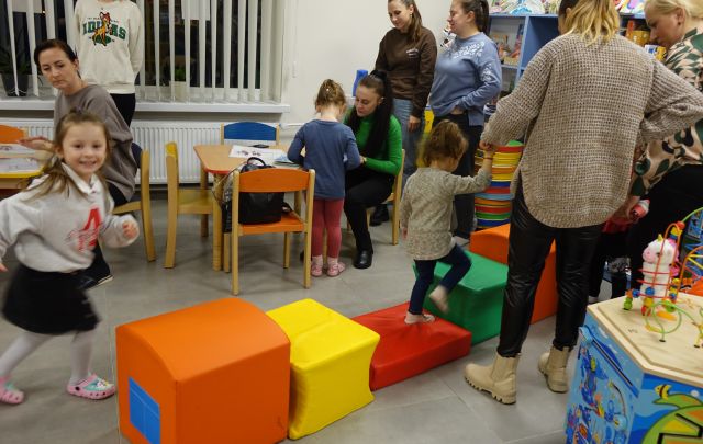 dzieci spacerują trzymane przez rodziców po kolorowych pufach