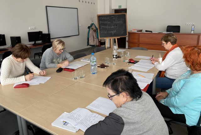 5 kobiet siedzi przy połączonych stołach i notuje