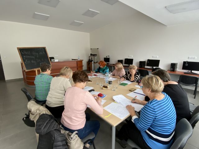 9 seniorek siedzi przy stołach i uczy się języka angielkskiego