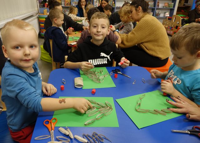 uśmiechnięty chłopiec, na stoliku naklejone gałązki z choinki z rolek po papierze toaletowym