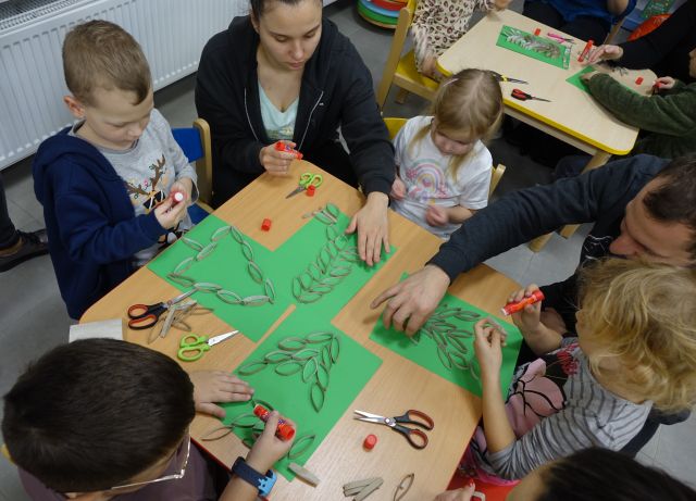 dzieci przy pomocy rodziców wyklejają na kartkach choinki z rolek po papierze toaletowym