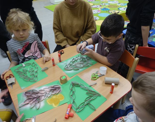 dzieci przy pomocy rodziców wyklejają na kartkach choinki z rolek po papierze toaletowym