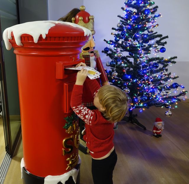 chłopiec w czerwonym sweteku wrzuca list do czerwonej skrzynki