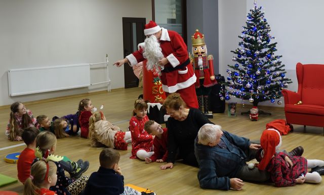 dzieci i dwie osoby dorosłę poupadały na podłogę bawiąc się w wyrywanie rzepki, przed nimi stoi Mikołaj