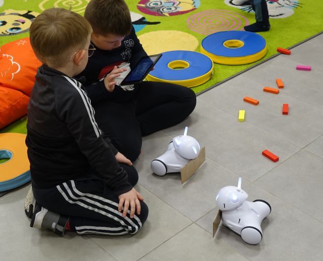 dwoje dzieci steruje robotami Photon jeżdżącymi po podłodze