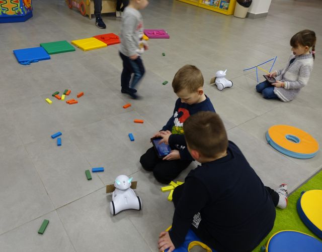 dzieci sterują robotami Photon przy użyciu tabletów, na podłodze porozkładane klocki LEGO