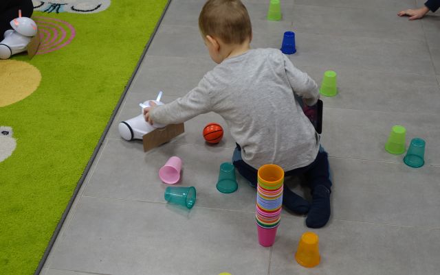 chłopiec steruje robotwm Photon jeżdżącym po podłodze pomiędzy kolorowymi kubeczkami