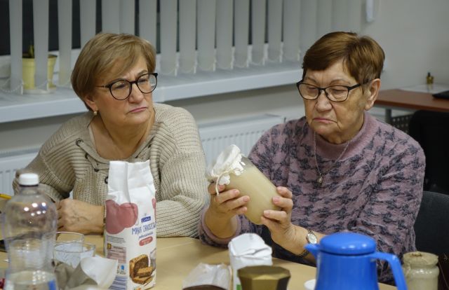 kobieta trzyma w dłoniach słoik z zakwasna słoikem, druga kobieta patrzy