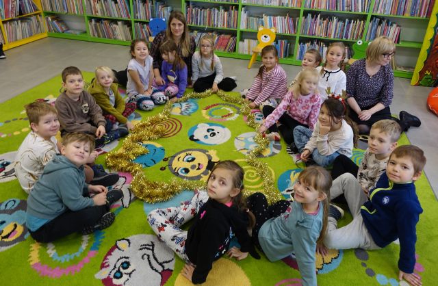 przedszkoalki siedzące na kolorowym dywanie prezentują ułożoną ze złotego łąńcucha na dywanie choinkę