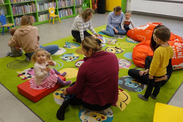 mamusie i małę dzieci siedzą na kolorowym dywanie i oglądają książki