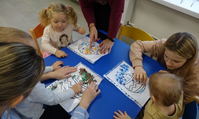 małę dzieci dekorują namalowane bombki kulkami