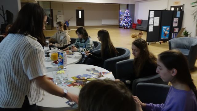 młodzież siedzi na siwych fotelach przy białych okrągłych stołach i ogląda karty Dixit