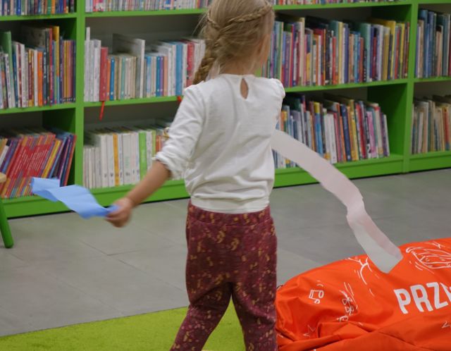 dziewczynka tańczy z dwoma paskami bibuły w kolorze białym i niebieskim