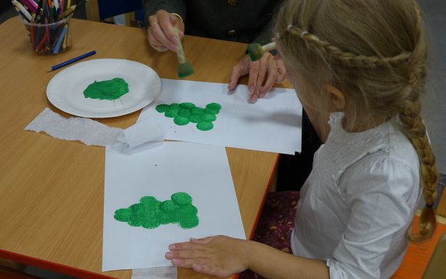 dziewczynka z mamą przybijają pieczątki na kartce, tworząc zieloną choinkę