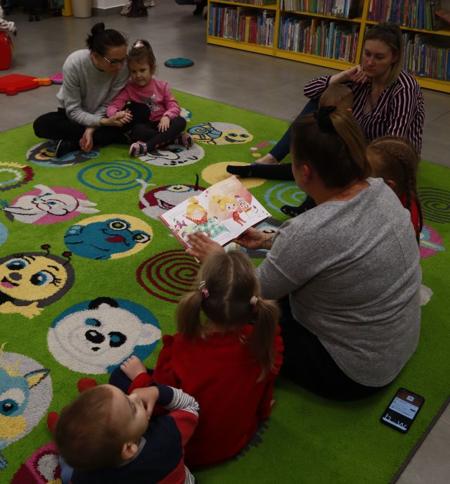bibliotekarka czyta dzieciom siedzącym na kolorowym dywanie