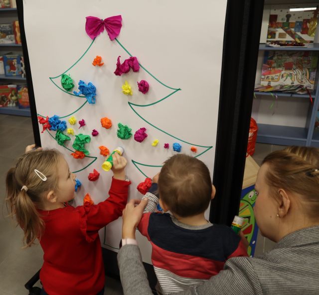 dzieci wyklejają na białym brystolu bombkami z kulek z bibuły choinkę