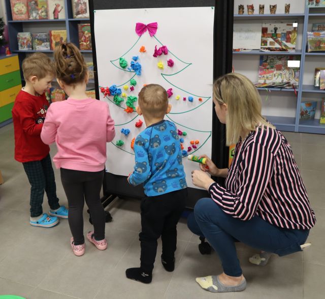 dzieci wyklejają na białym brystolu bombkami z kulek z bibuły choinkę