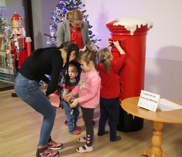 dzieci stoją przed skrzynką na listy, dziewczynka wrzuca list do mikołąja
