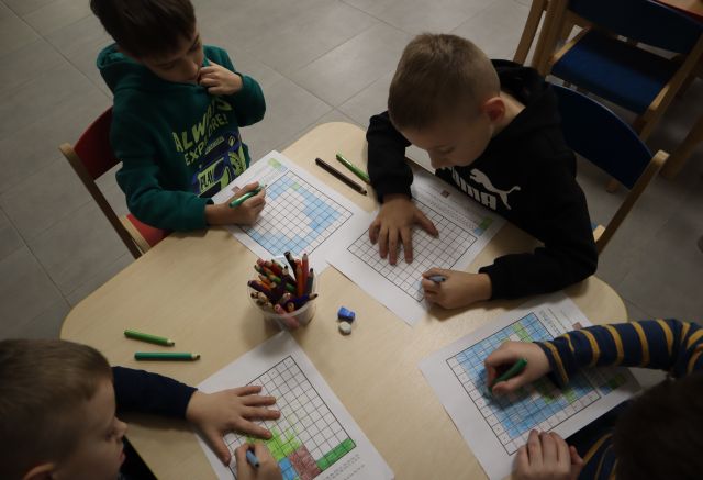 4 chłopców zamalowuje na kartkach kratki tak by powstała choinka