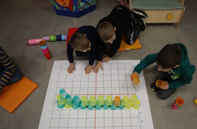 3 chłopców układa wieżę z kolorowych kubeczków