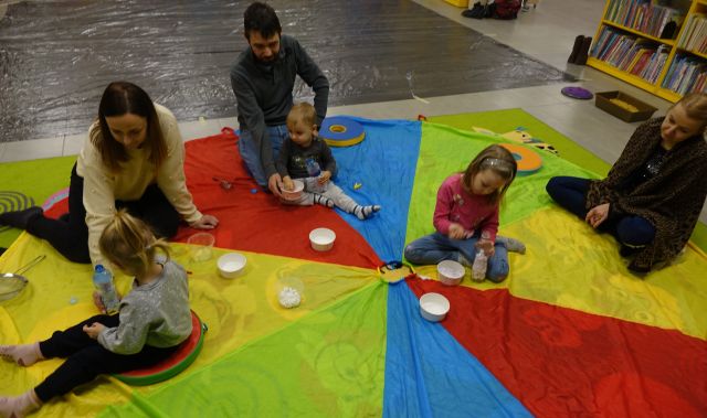 dzieci i rodzice wkładają małe białe kulki do butelek