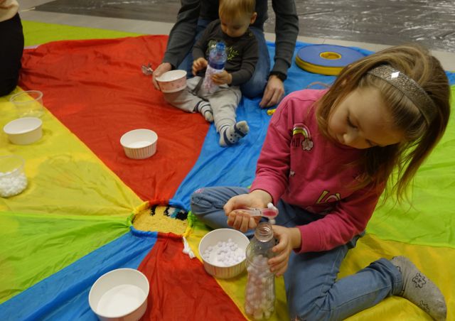 dzieci i rodzice wkładają małe białe kulki do butelek