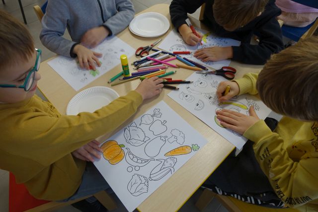 dzieci siedzące przy stolikach malują owoce i warzywa