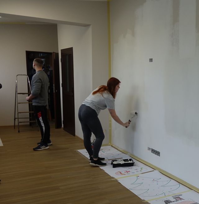 dziewczyna maluje ścianę, w tle stoi chłopak