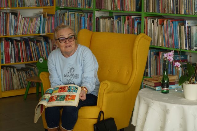 starsza kobieta siedzi na żółtym fotelu z książką