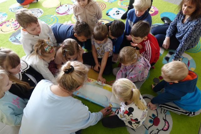 dzieci i kobieta oglądają na dywanie książkę rozkładankę