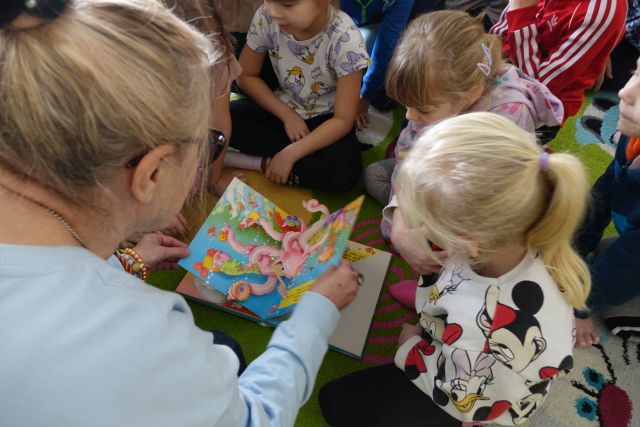 dzieci i kobieta oglądają na dywanie książkę rozkładankę