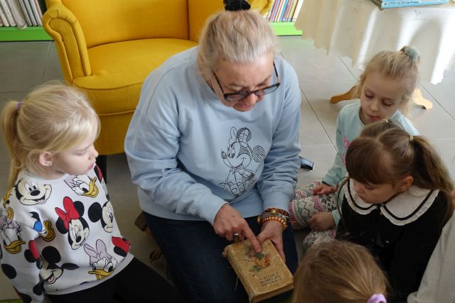 kobieta kucająca na kolorowym dywanie pokazuje dzieciom książkę