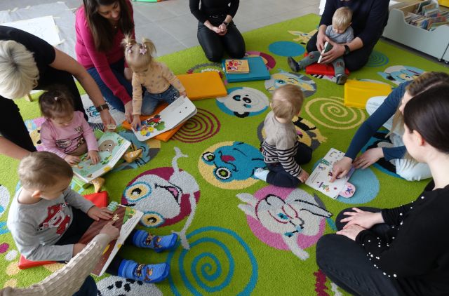 małe dzieci i rodzice siedzą na kolorowym dywanie i oglądają książki