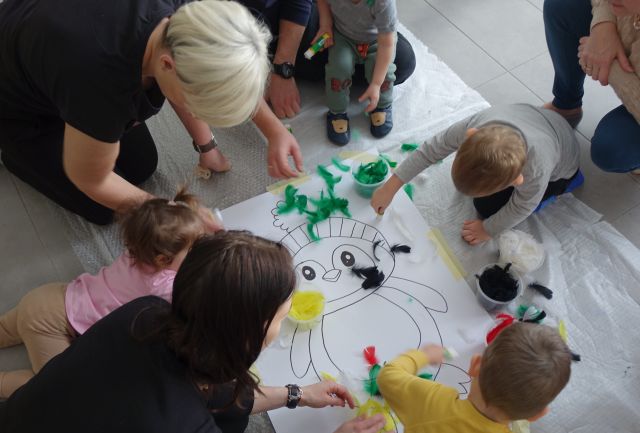 dzieci i rodzice wyklejają kolorowymi piórami pingwina