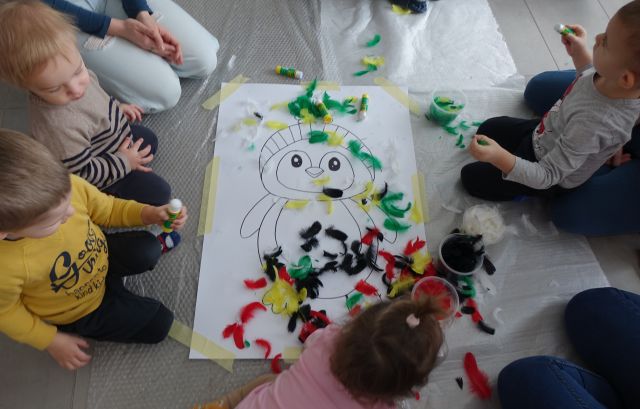 małe dzieci z rodzicami wyklejają kolorowymi piórami pingwiny