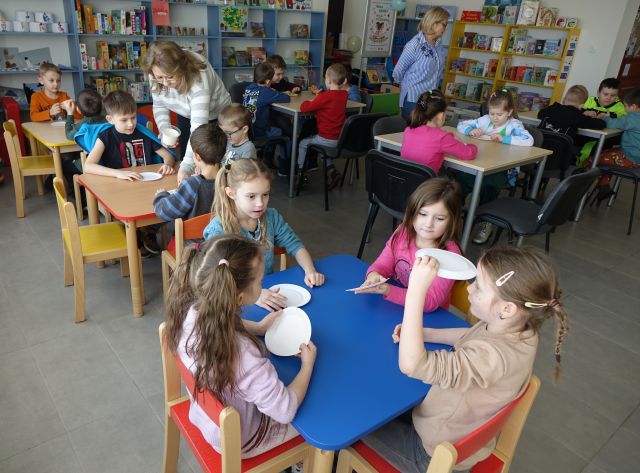 przedszkolaki siedzą przy stolikach, na któych leżą papierowe talerzyki
