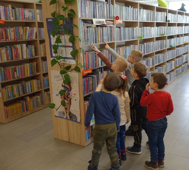 przedszkolaki oglądają książki na regale w bibliotece