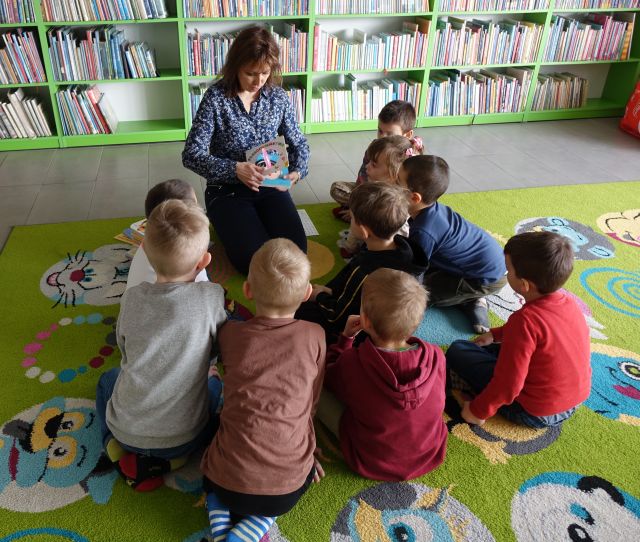 dyrektorka biblioteki pokazuje dzieciom siedzącym na kolorowym dywanie książki