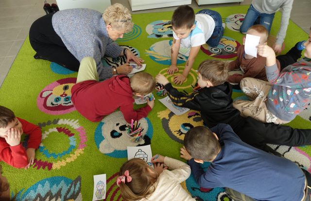 dzieci siedzą i leżą na kolorowym dywanie i kolorują obrazki